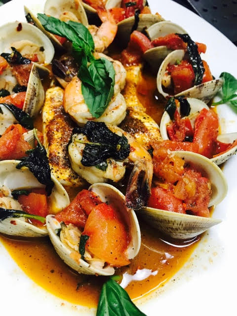 Clams with tomatoes and basil on a white plate.