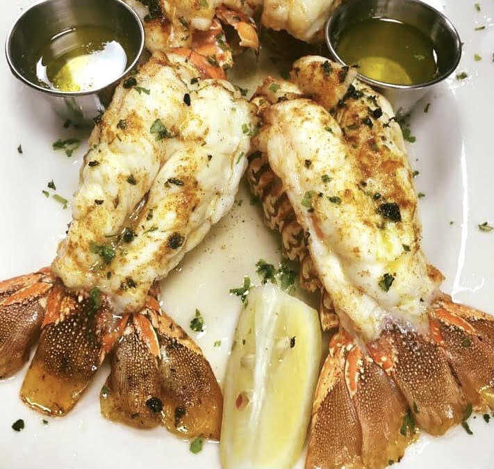 Three lobster tails on a plate with lemon wedges.