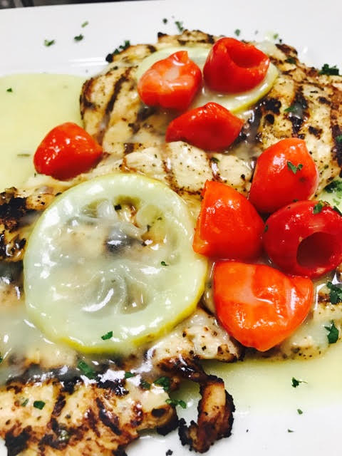 Grilled chicken with lemon and tomatoes on a white plate.